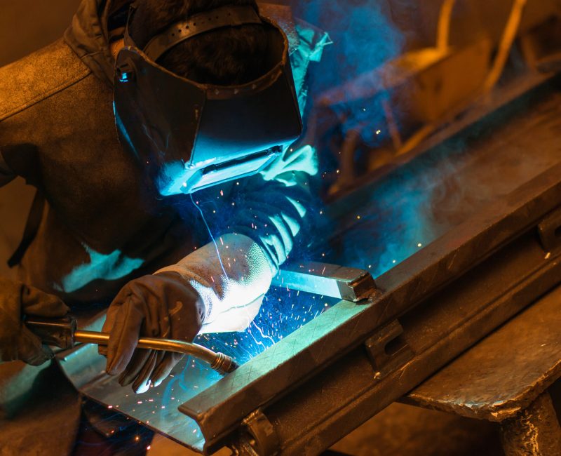 Young man with protective mask welding in a factory
